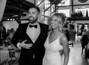 A couple in formal attire laughing together at an indoor wedding reception venue.