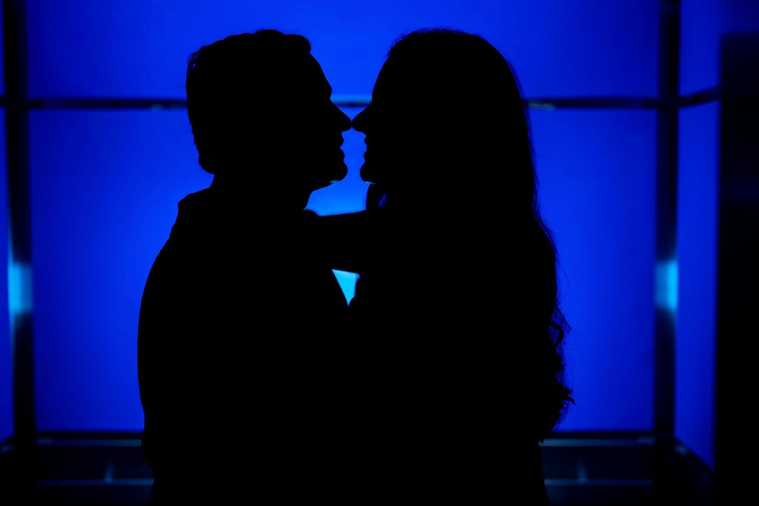 Romantic silhouette of a couple against a blue backlit background creating an intimate mood.