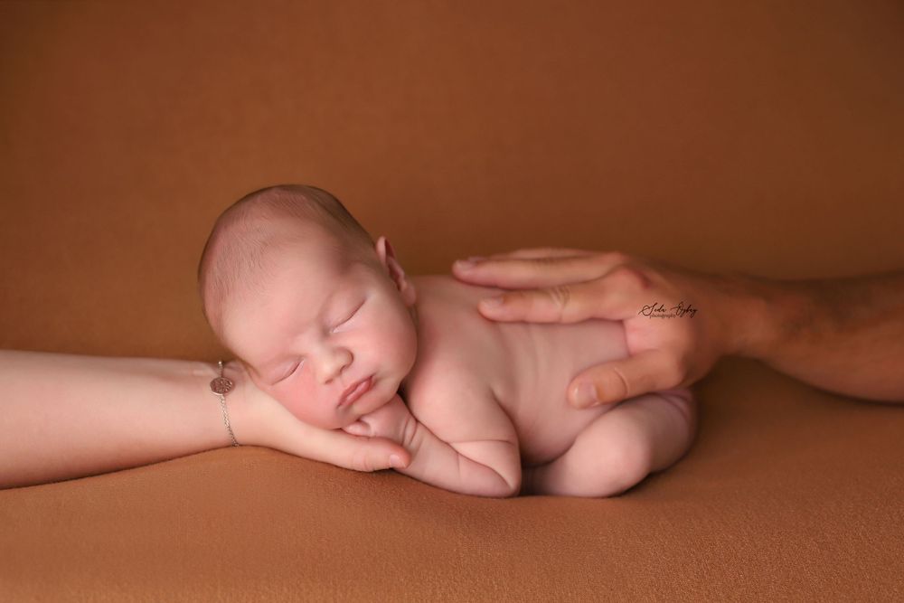 Natural newborn photography session with gentle poses on brown backdrop.