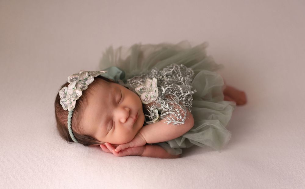 Artistic newborn portrait with soft mint tulle dress against neutral background.