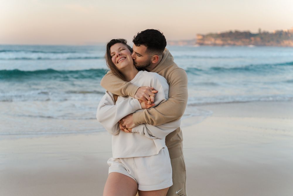 A loving couple embraces on Bondi beach at sunrise with ocean waves and coastal scenery in the background during a Sydney Photoshoot