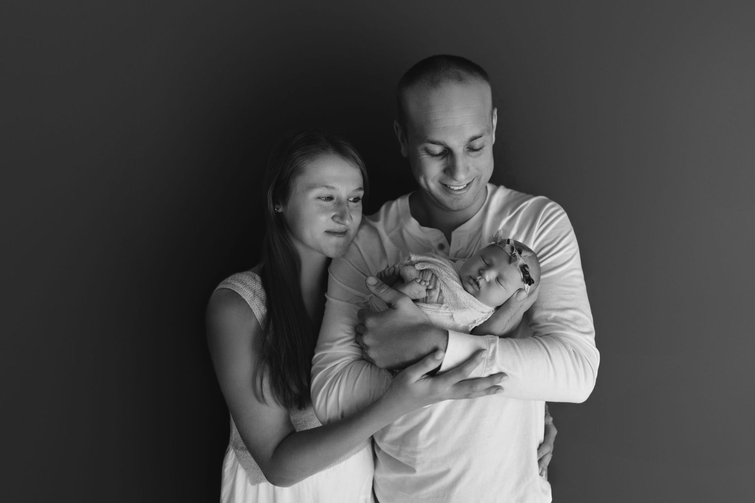 A tender black and white photo series showing a couple embracing and cradling their newborn baby.