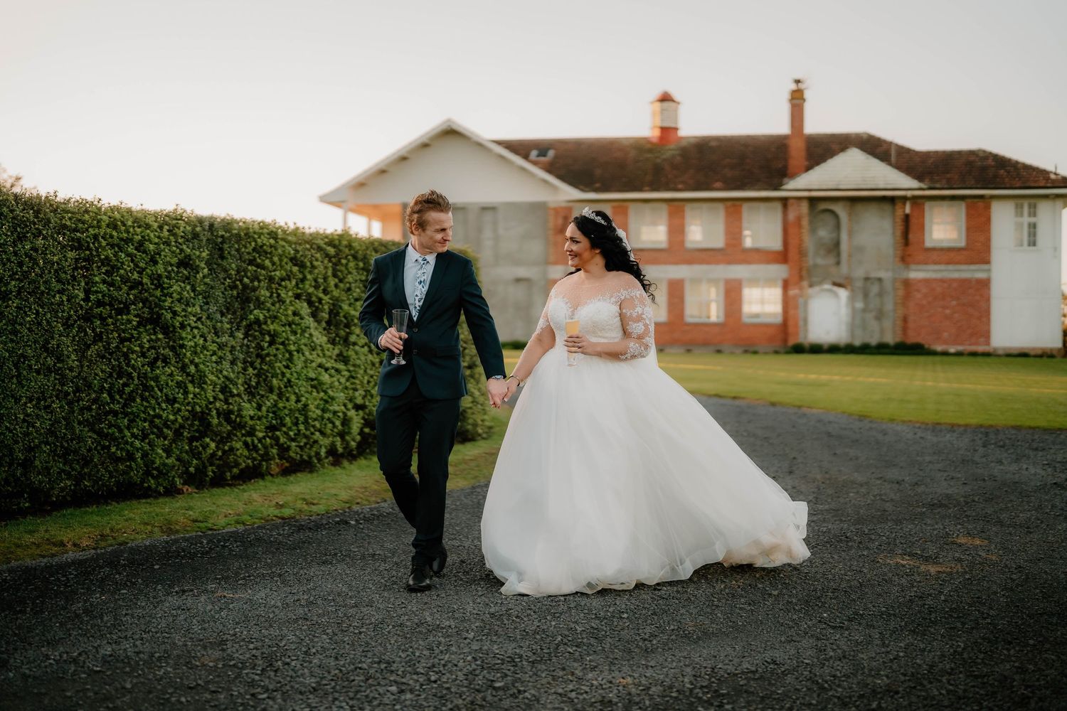 A bride and groom walk hand in hand down a paved pathway during their outdoor wedding celebration.