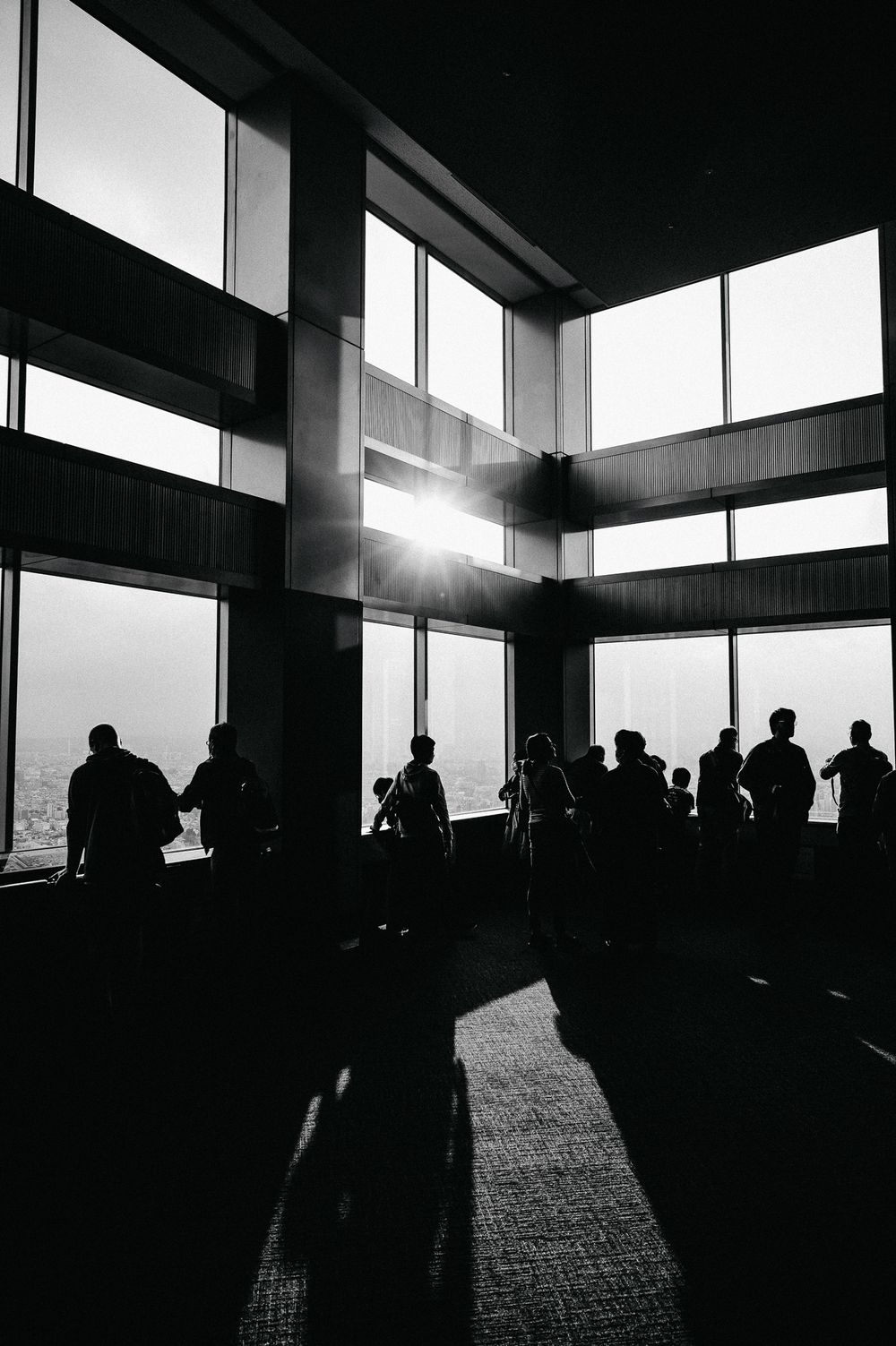 Silhouettes of people stand against bright windows in a dark architectural space creating a dramatic contrast effect.
