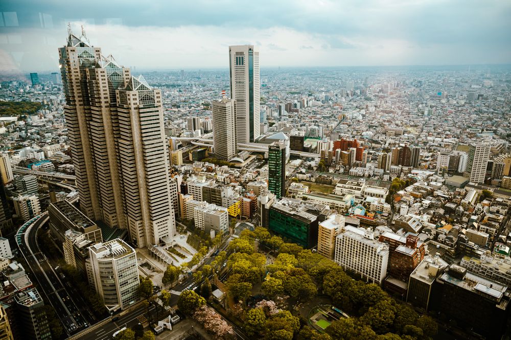 Aerial panoramic cityscape view of Tokyo showing modern skyscrapers, residential buildings and urban sprawl on a cloudy day.