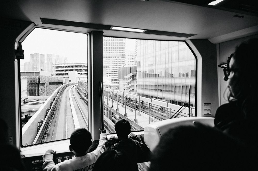 View of empty train tracks through the window of a moving train car in an urban setting.