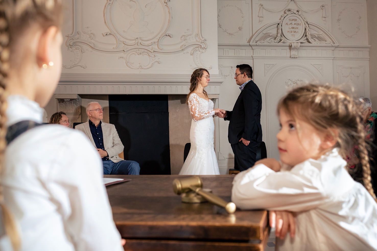 Kinderen wachten op hun moment tijdens de ceremonie terwijl het bruidspaar hand in hand op de achtergrond staat