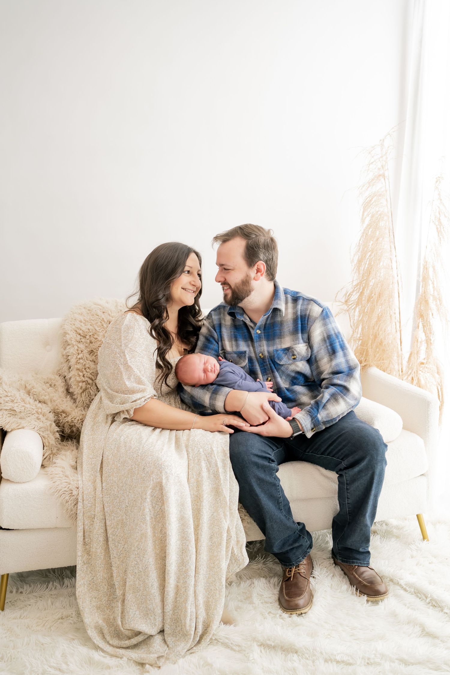 Couple lounges on cream colored couch while sharing intimate moments in softly lit studio setting.