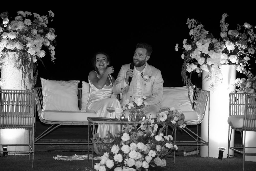 A black and white photo showing bride and groom seated at a table surrounded by flowers