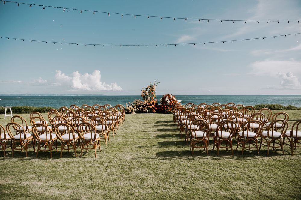 Wooden chairs arranged on a scenic oceanfront lawn for an outdoor wedding ceremony setup.