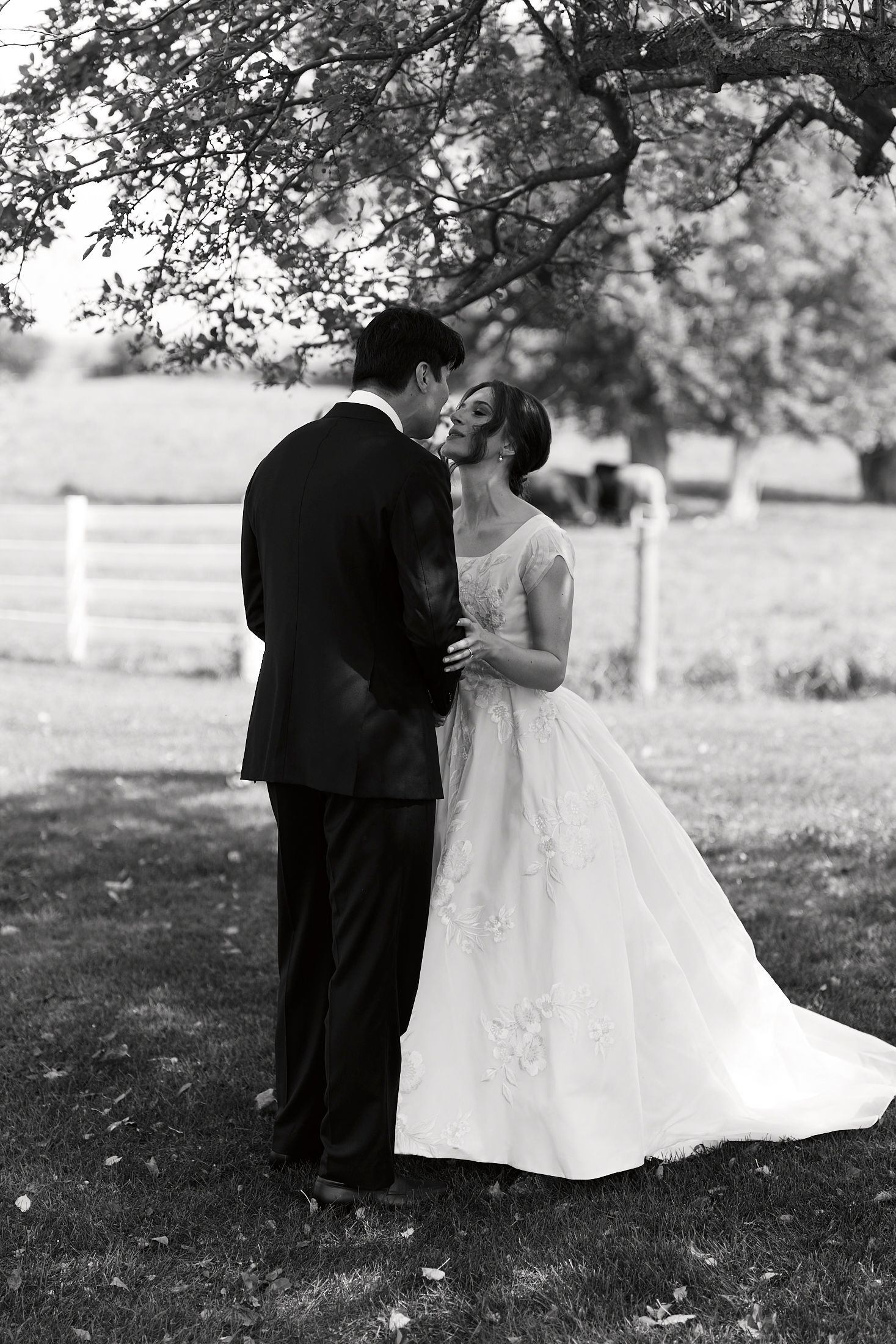 Black and white wedding portrait showing couple in elegant attire dancing on garden grounds.