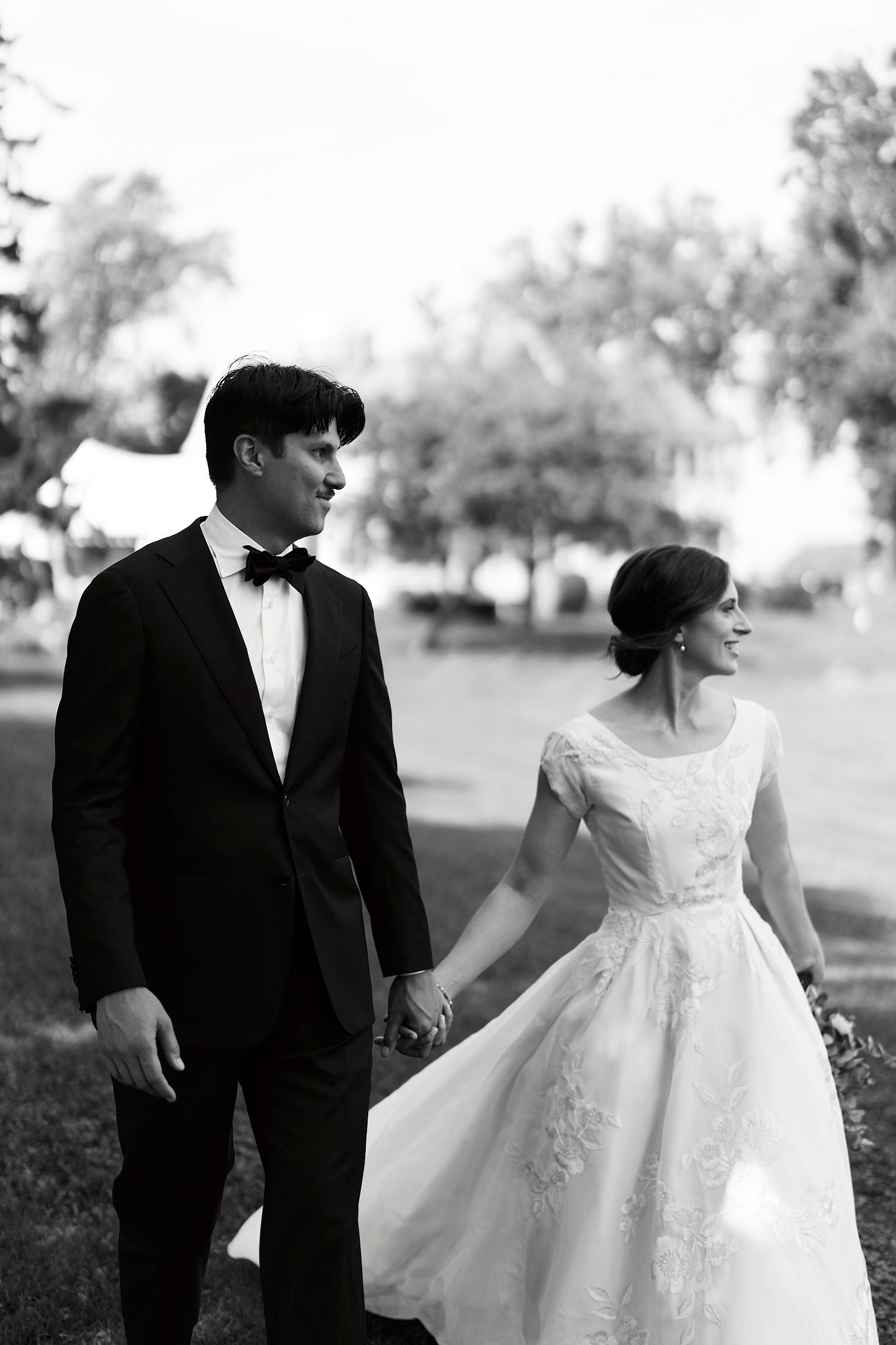 Elegant bride in flowing white gown and groom in tuxedo share intimate moment in outdoor setting.