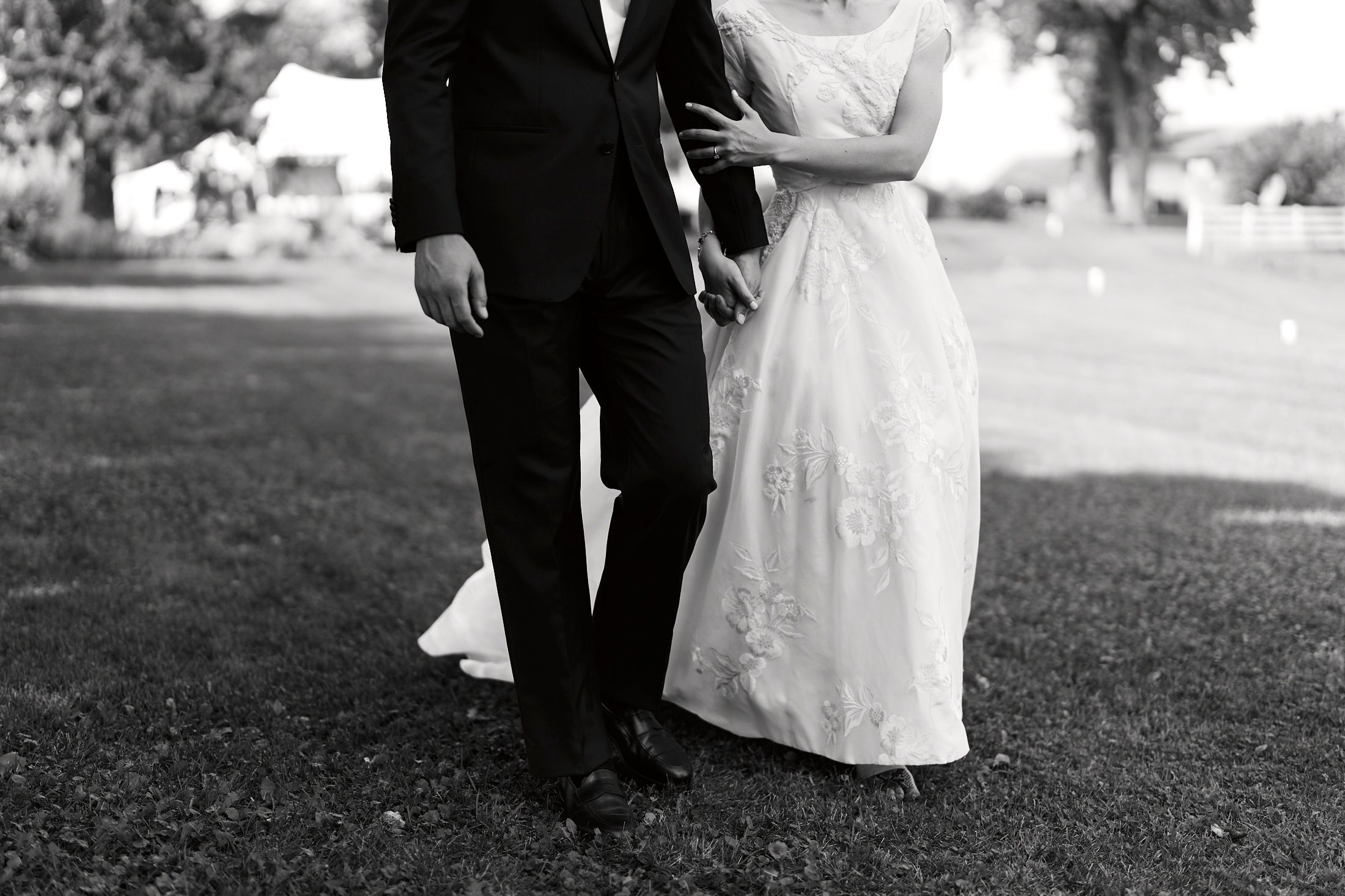A black and white wedding portrait of a couple standing together on a grassy slope.