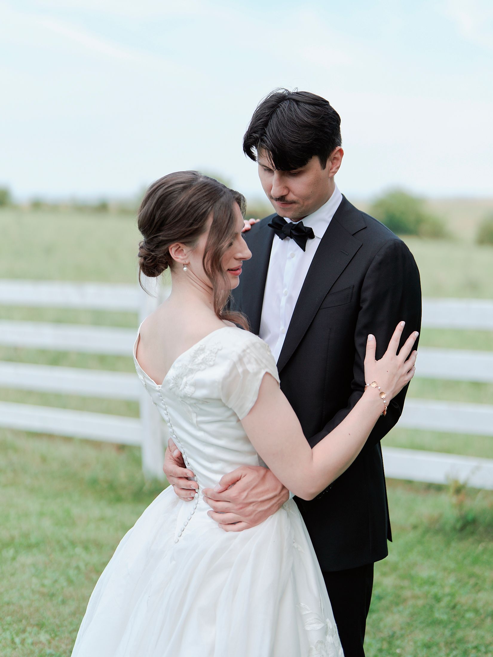 A couple in wedding attire embraces in front of a white fence on their special day.