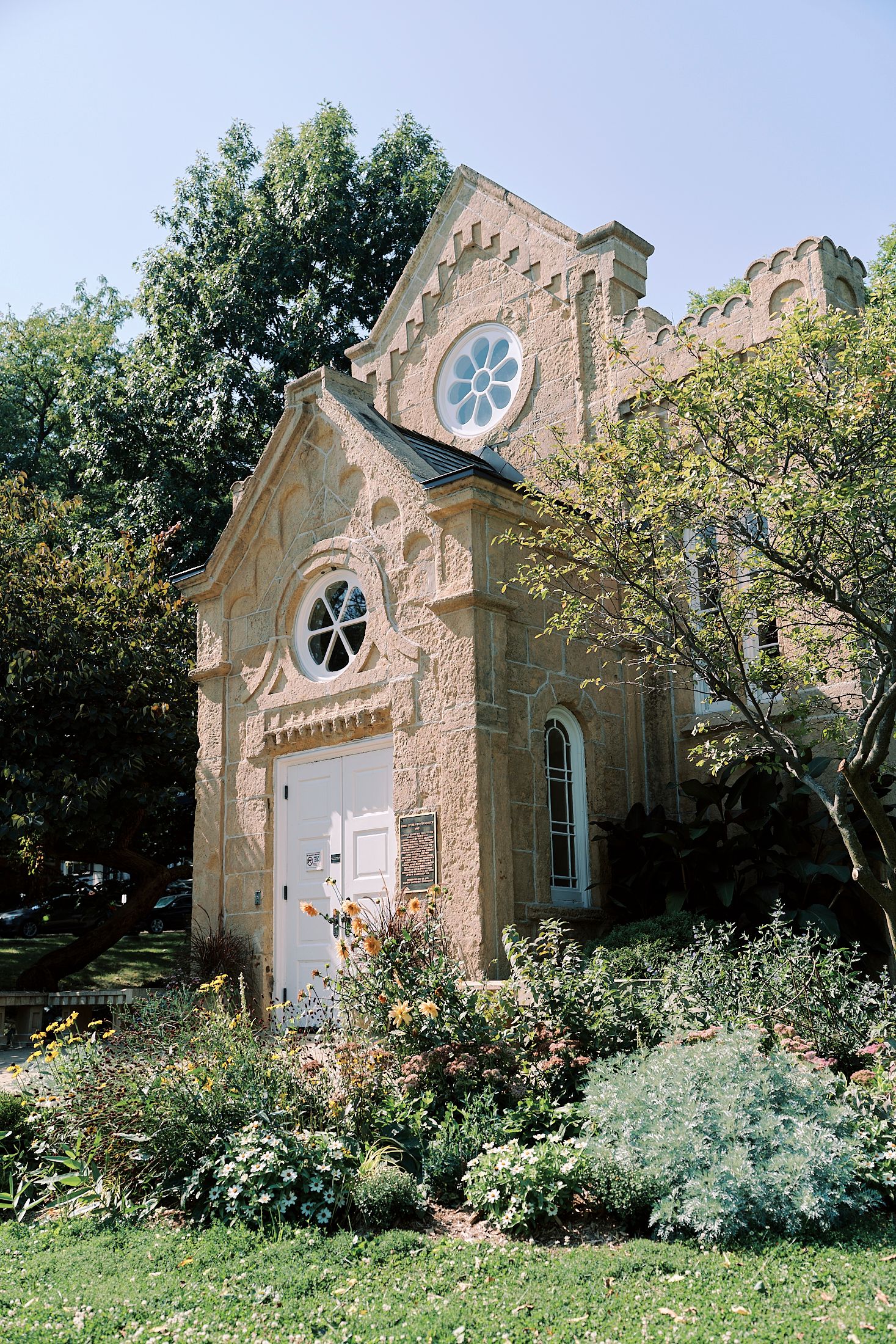 Small stone chapel with gothic window and flowering garden in the countryside.