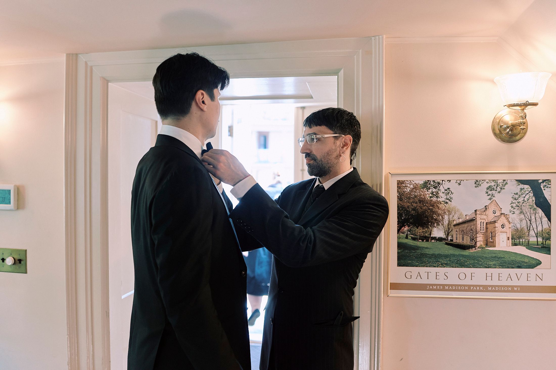 Wedding guests in formal attire gather in an elegant hallway with framed artwork on cream-colored walls.