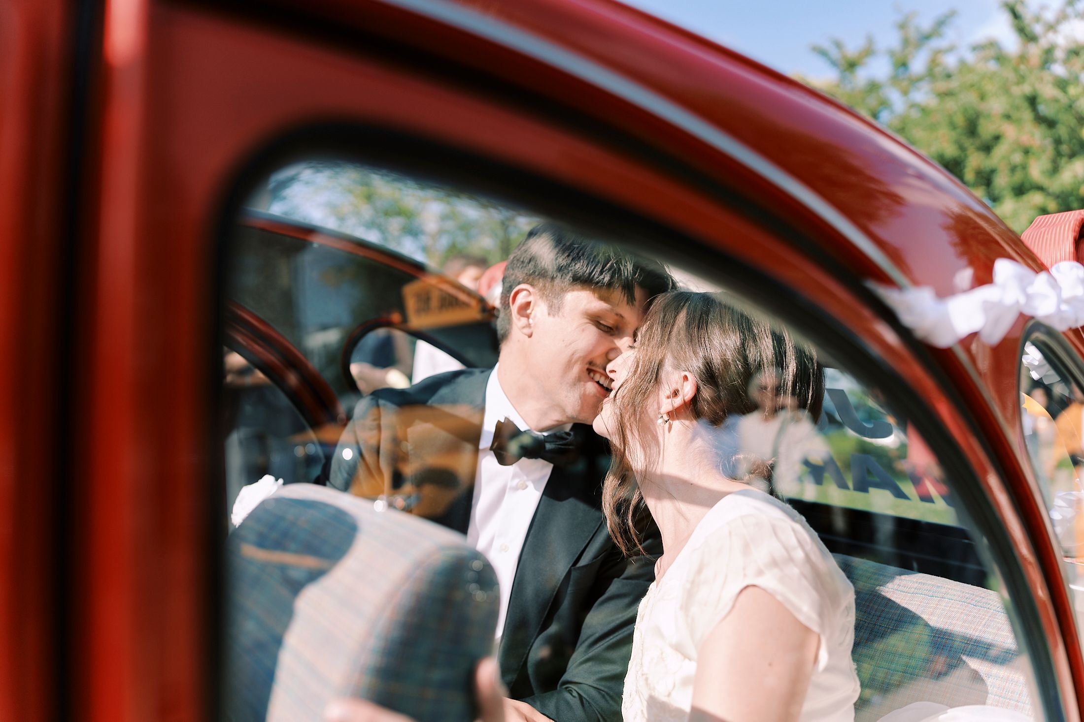Red car interior view shows wedding party members through the windshield on a sunny day.