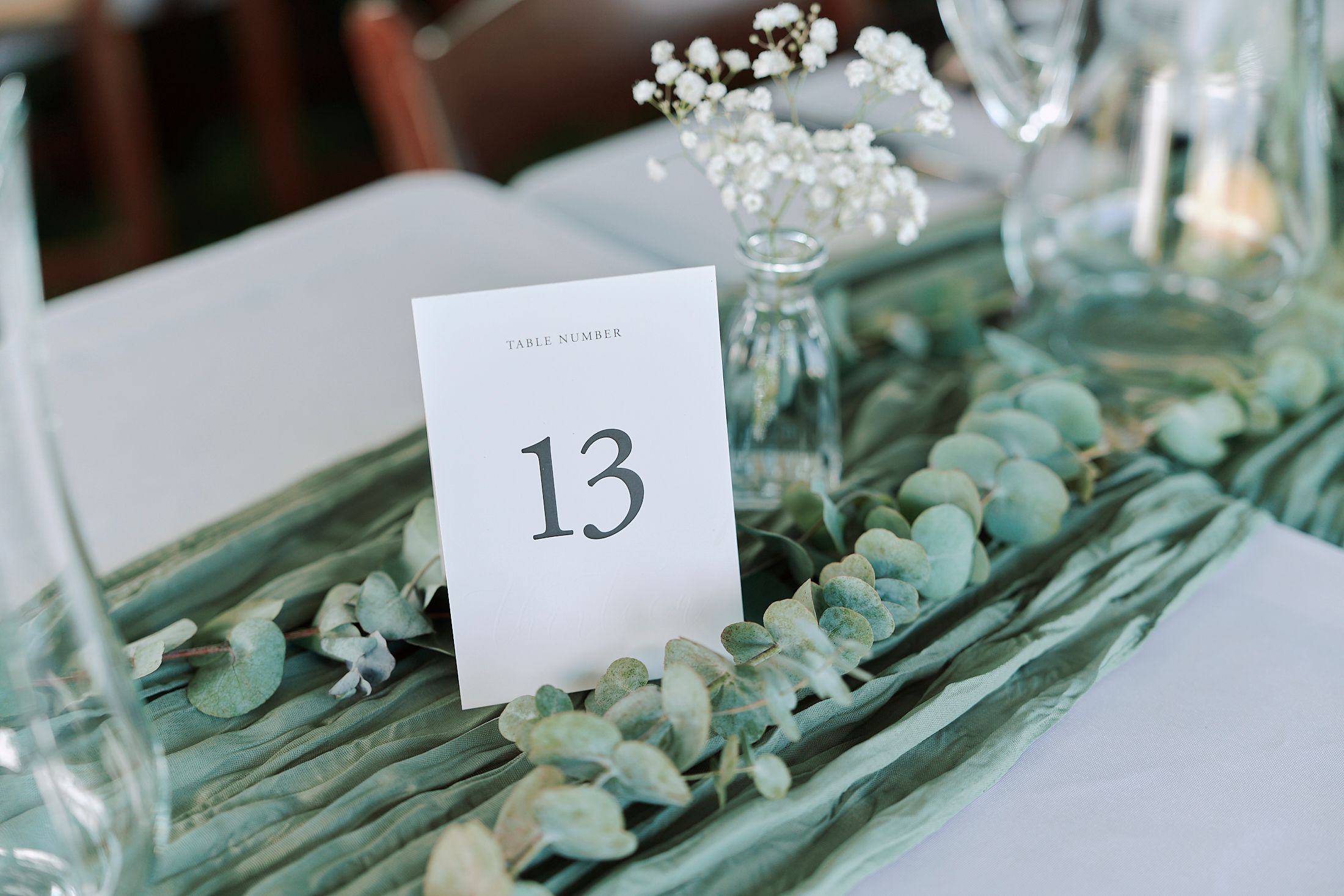 Wedding reception table numbers displayed among eucalyptus leaves and baby's breath.