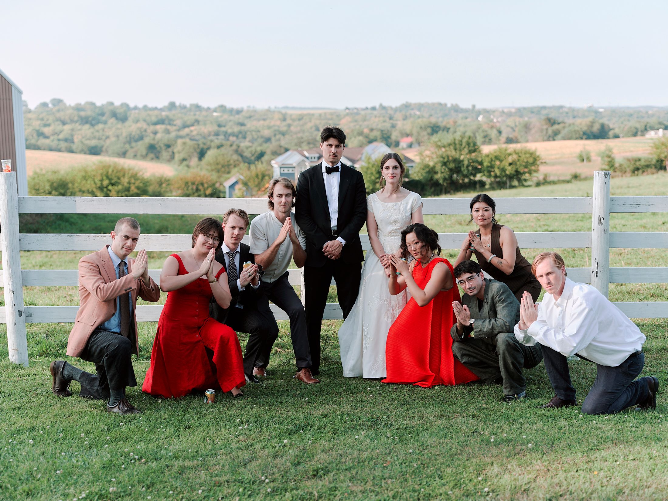 Wedding party posing on a grassy hillside with red and black attire.