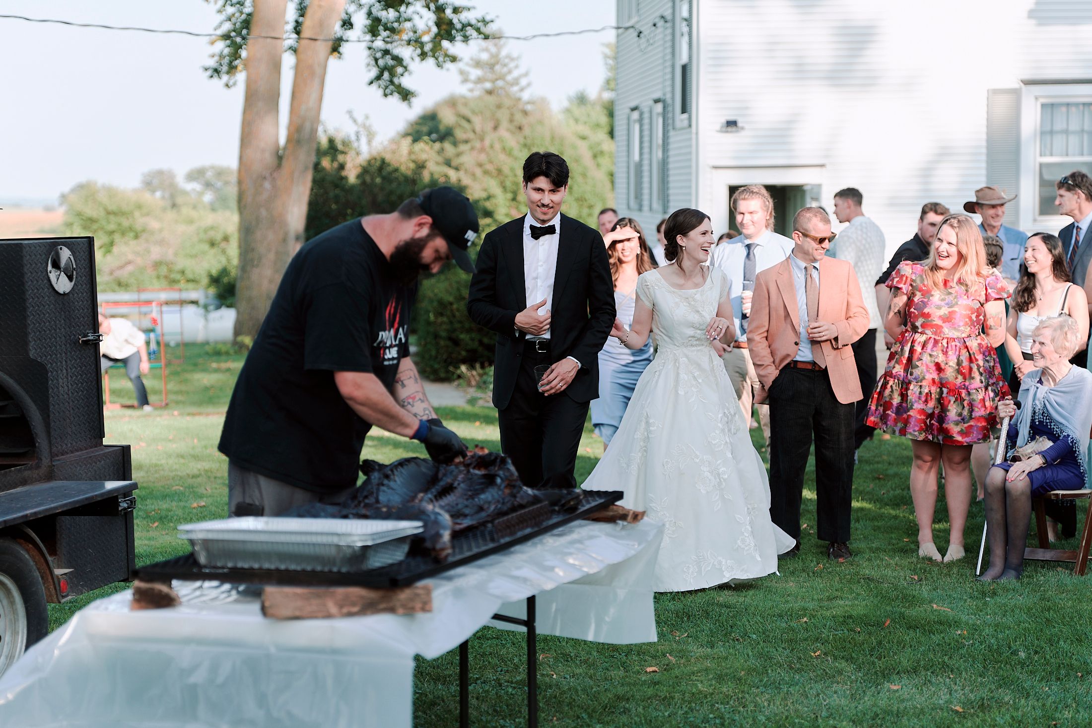 Wedding guests gather outdoors for a casual reception on a grassy lawn during a summer celebration.