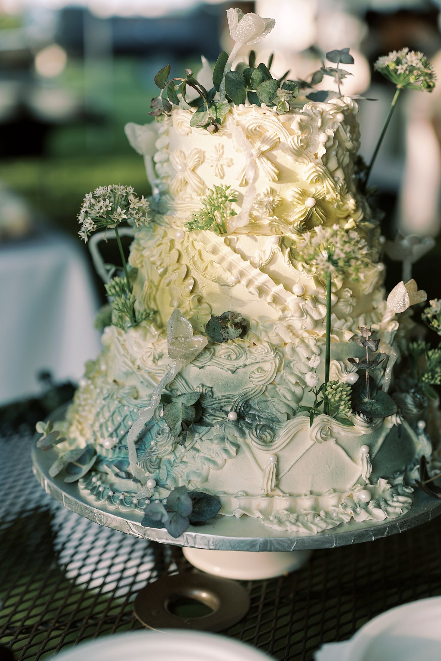 Close-up view of a white wedding cake with intricate piping and fresh floral decorations in soft lighting.