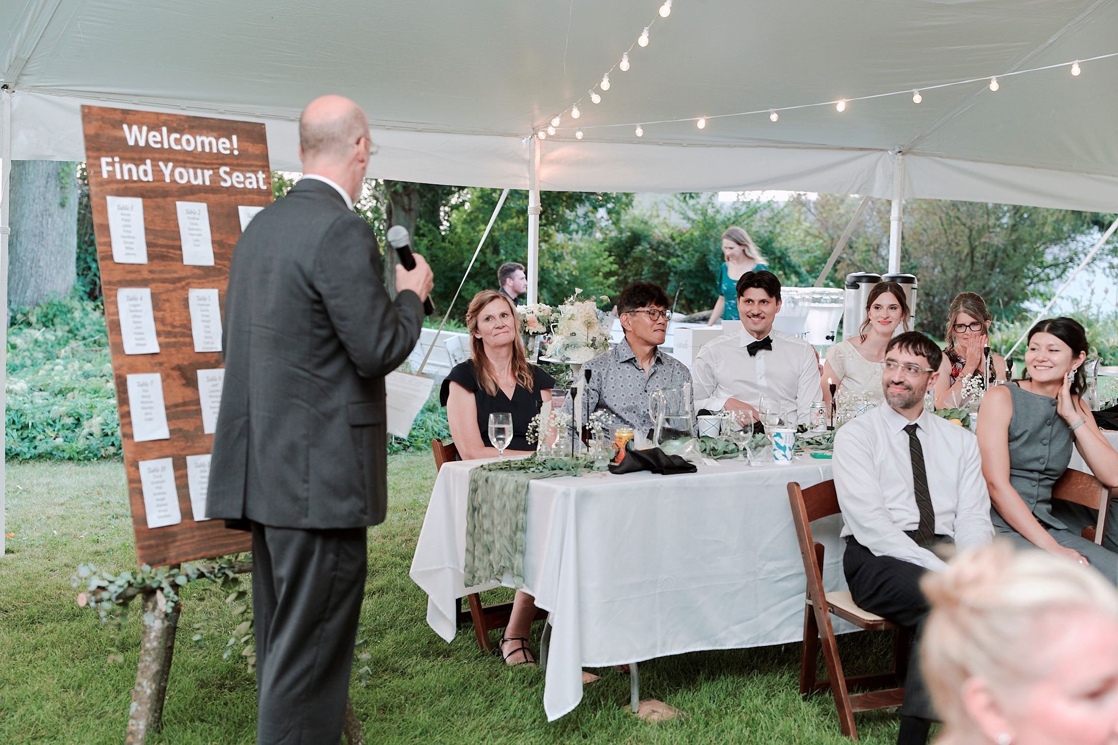 Wedding reception setup outdoors with string lights and rustic wooden decor.