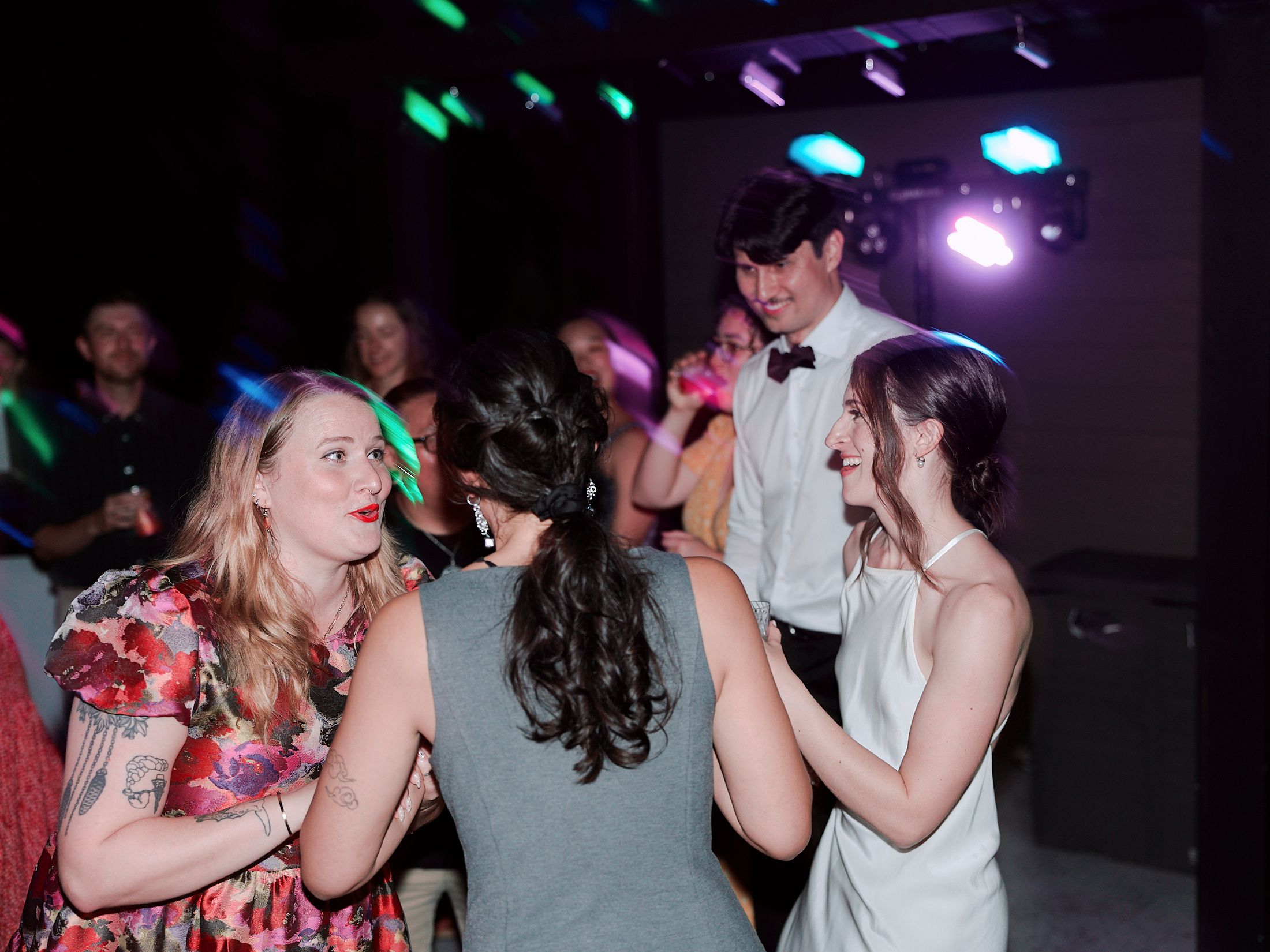 People dancing and socializing at a dimly lit party venue with colorful lighting effects.