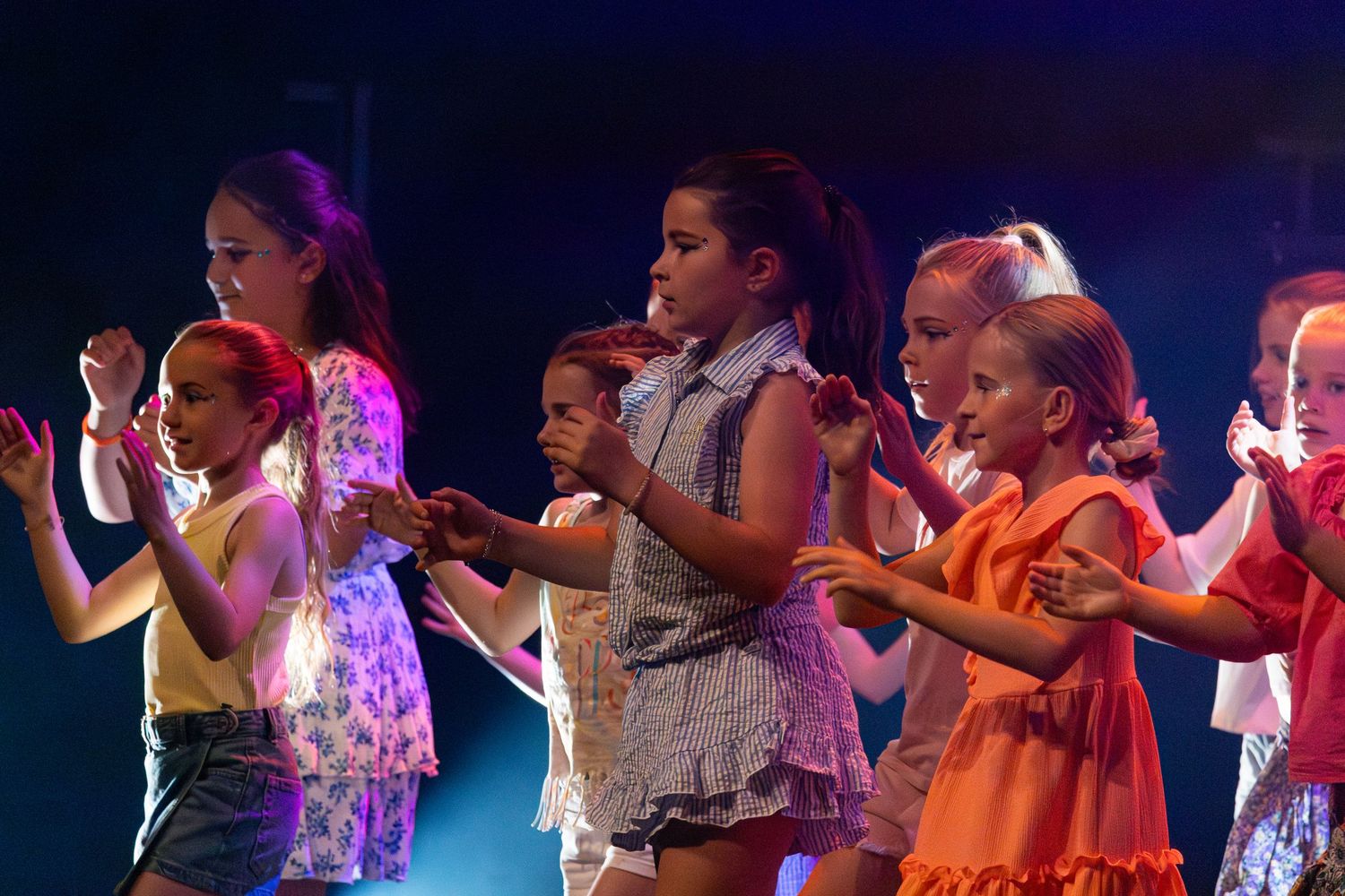Dancers perform energetic choreography on stage under colorful theatrical lighting during a live performance.