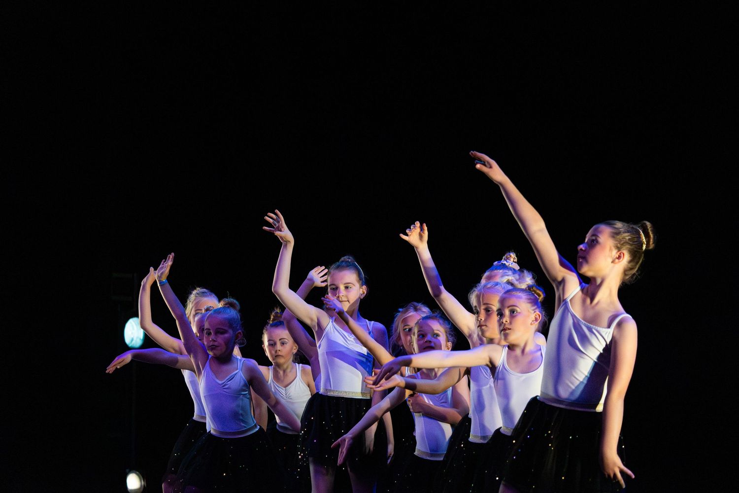 Dancers perform a synchronized contemporary dance sequence illuminated by blue stage lighting.