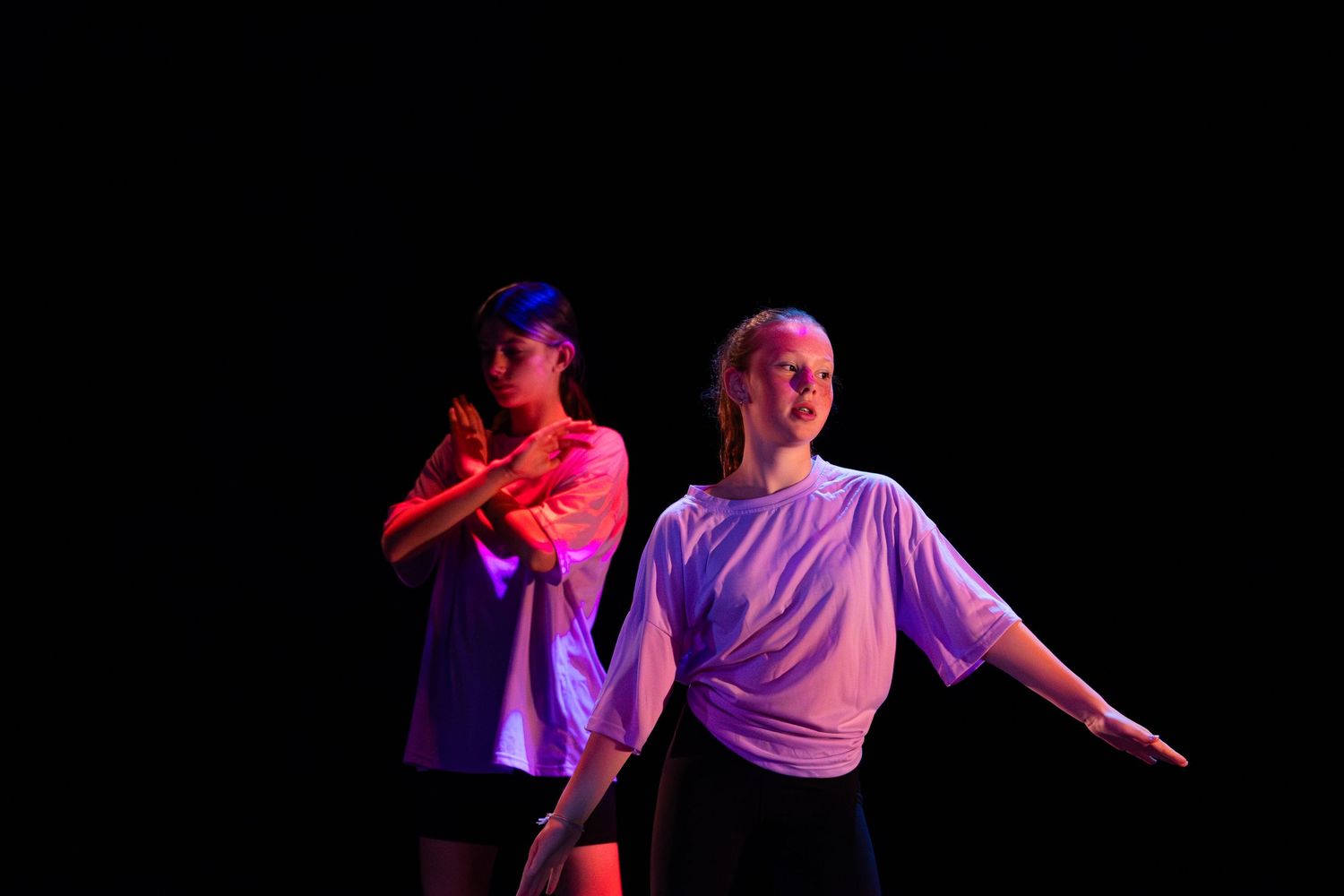 Dancers in white shirts perform a dynamic contemporary dance sequence under colorful stage lighting.