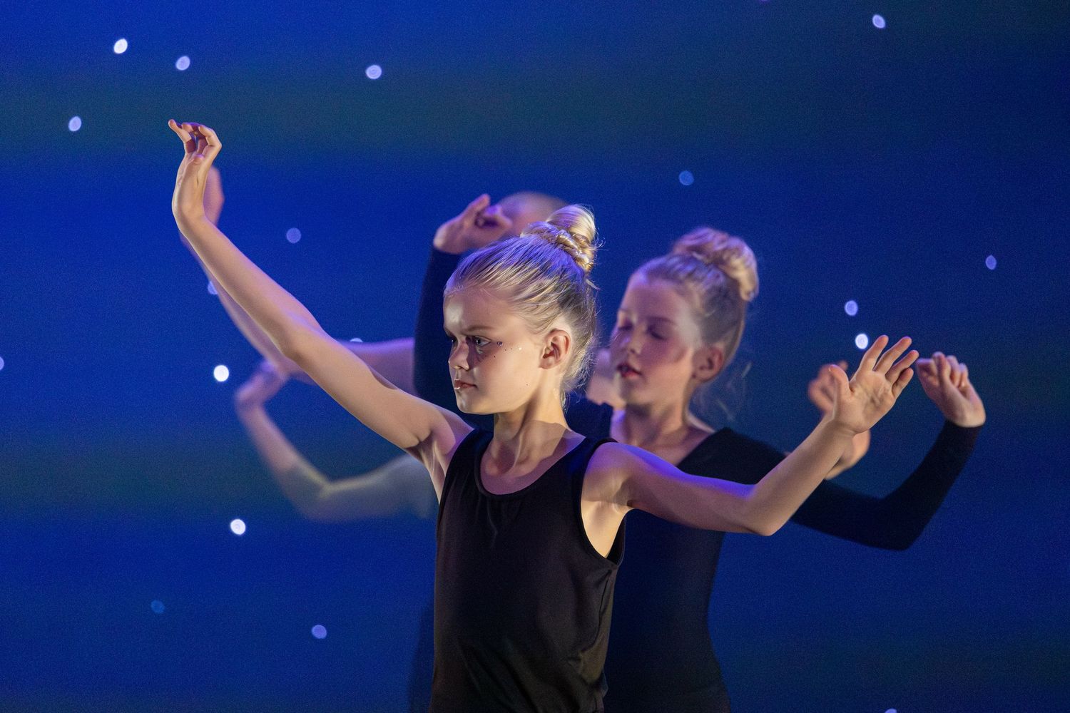 Contemporary dancers move in synchronized formation during a stage performance with blue lighting effects.