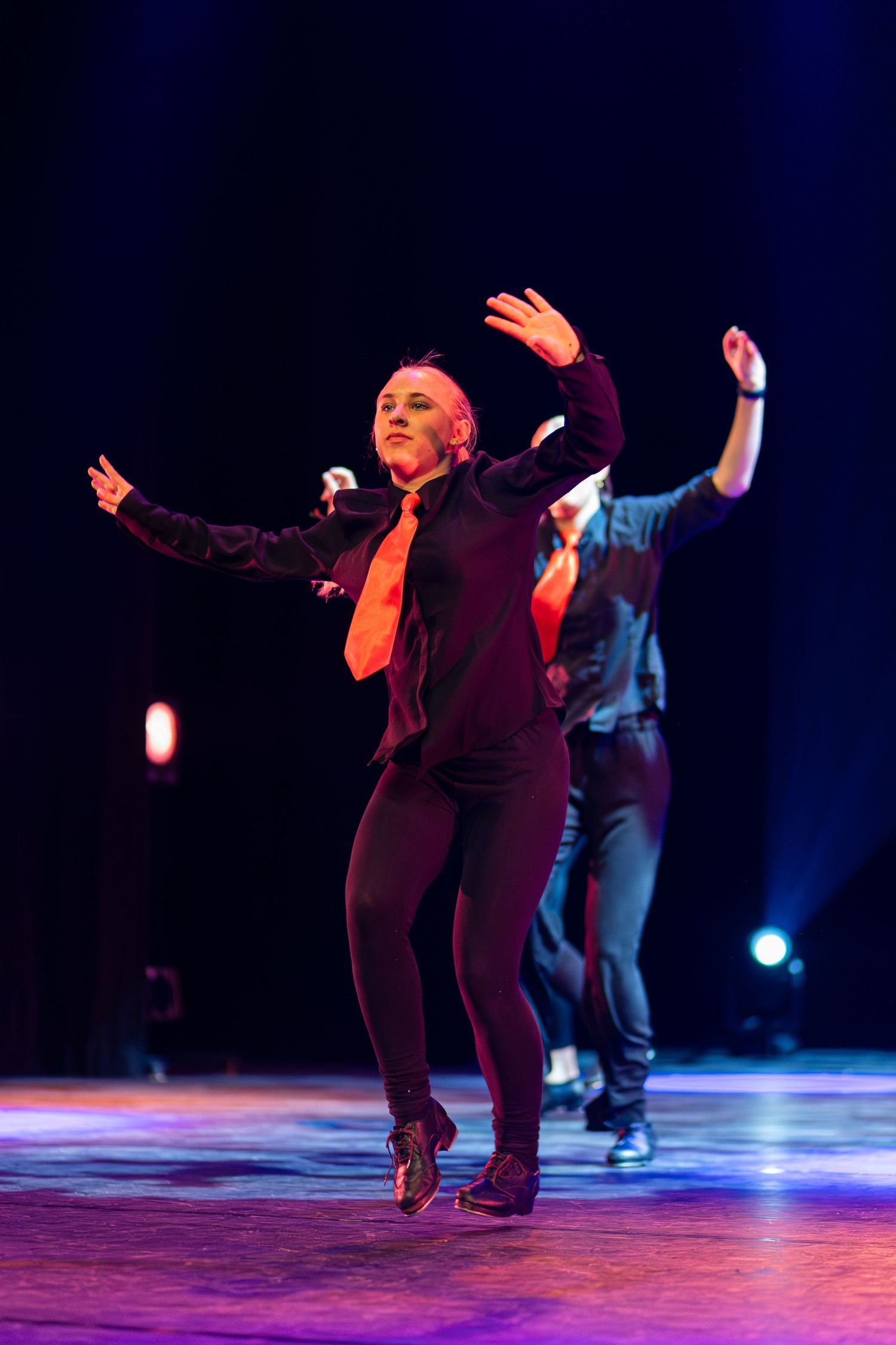 Performers in burgundy outfits dance energetically under blue stage lighting during a contemporary dance show.