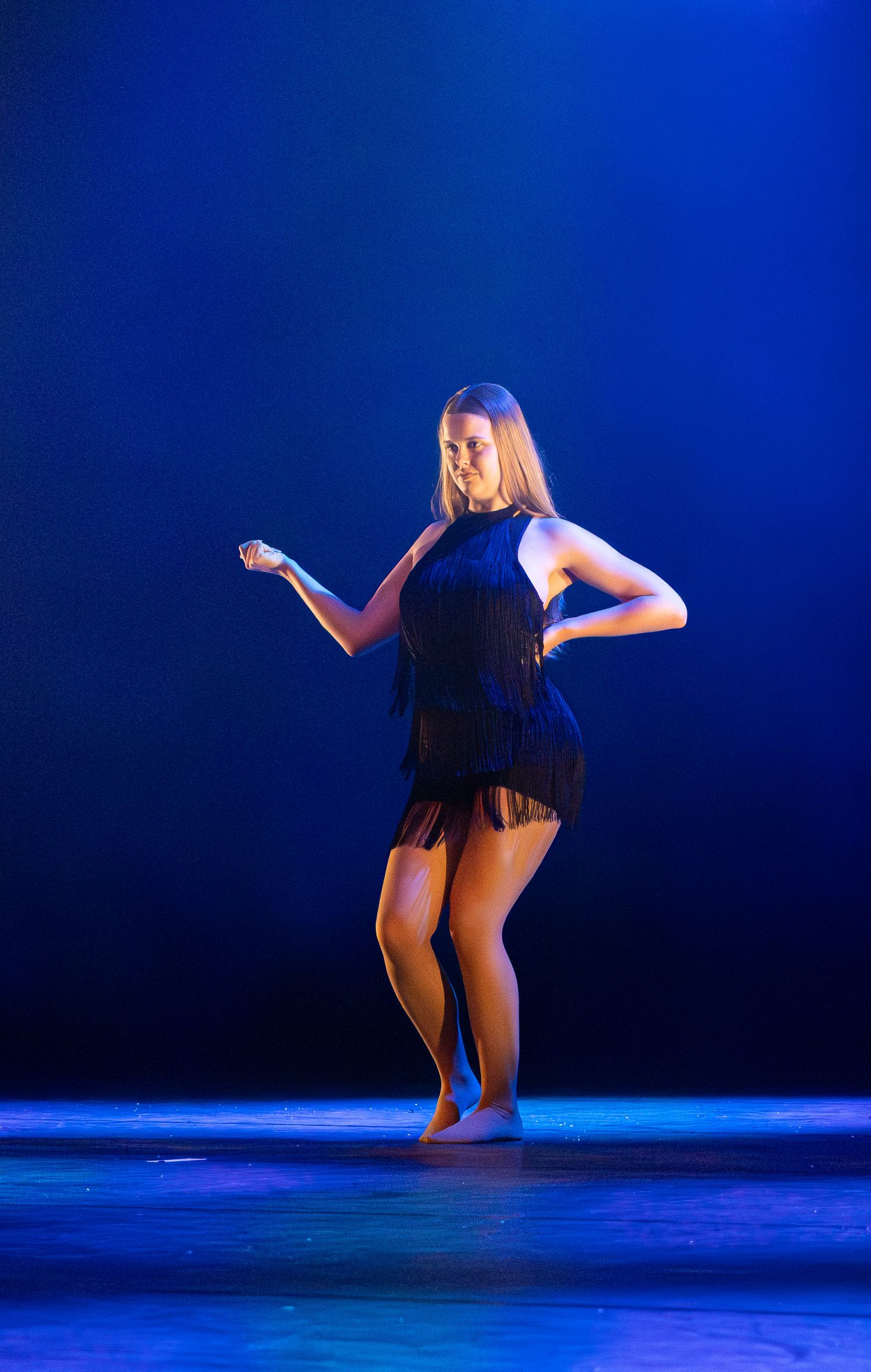 Contemporary dancers in black costumes perform expressive movements on a stage bathed in deep blue lighting.
