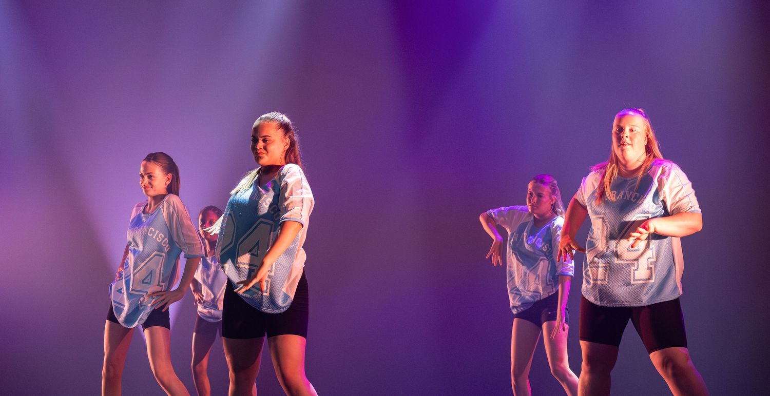 Two dancers perform a contemporary duet on stage with dramatic purple lighting.