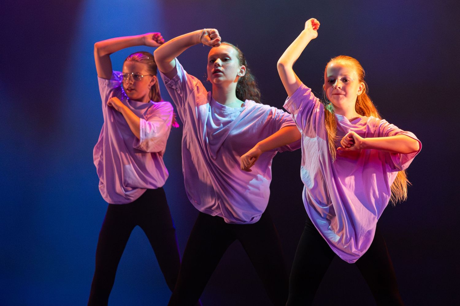 Dancers in flowing white shirts perform a synchronized modern dance routine under dramatic blue and purple lighting.