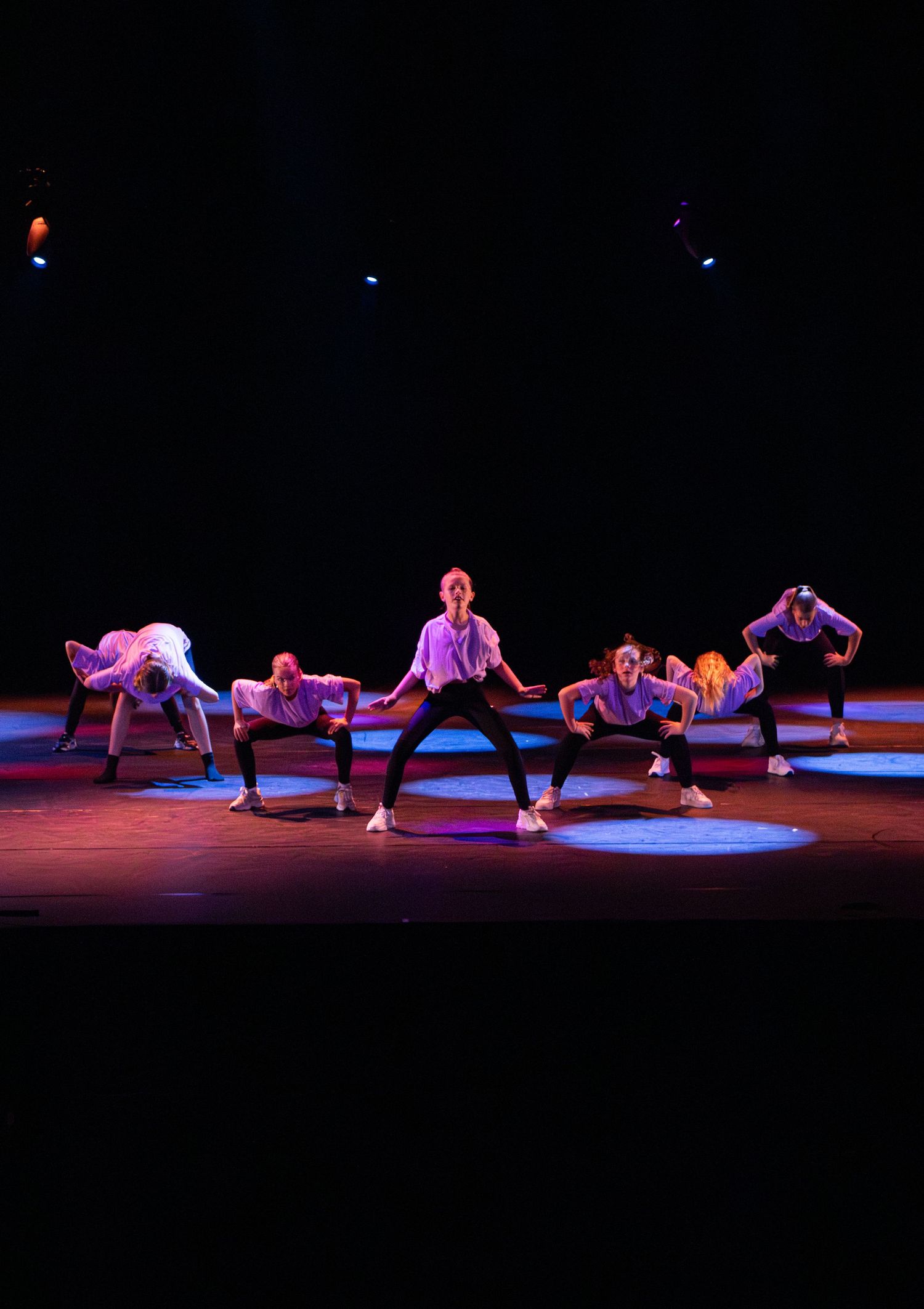 Dancers perform a contemporary dance piece on a dark stage illuminated by dramatic red and blue lighting.