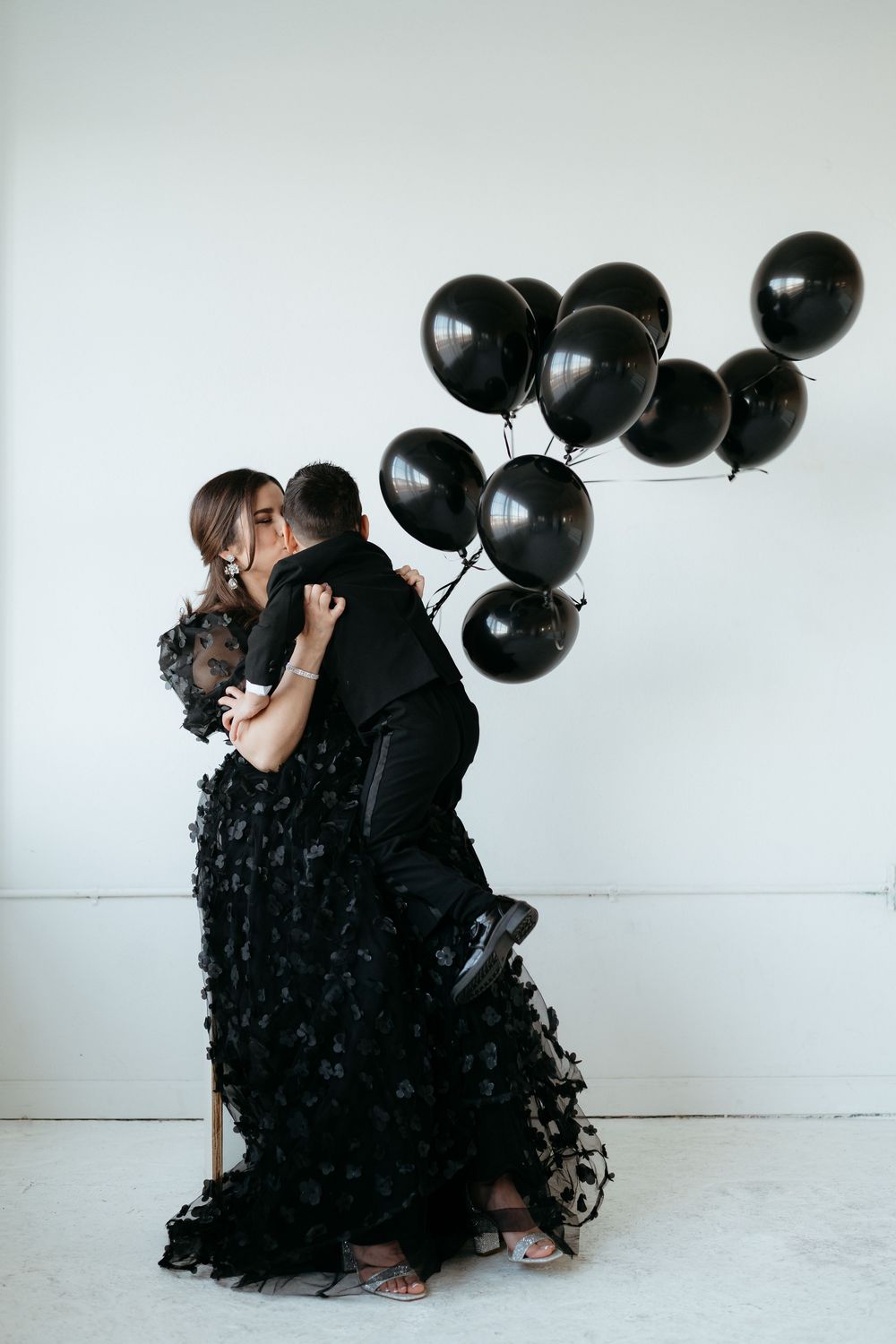 Elegant family photo session with black balloons and flowing dress against white background.