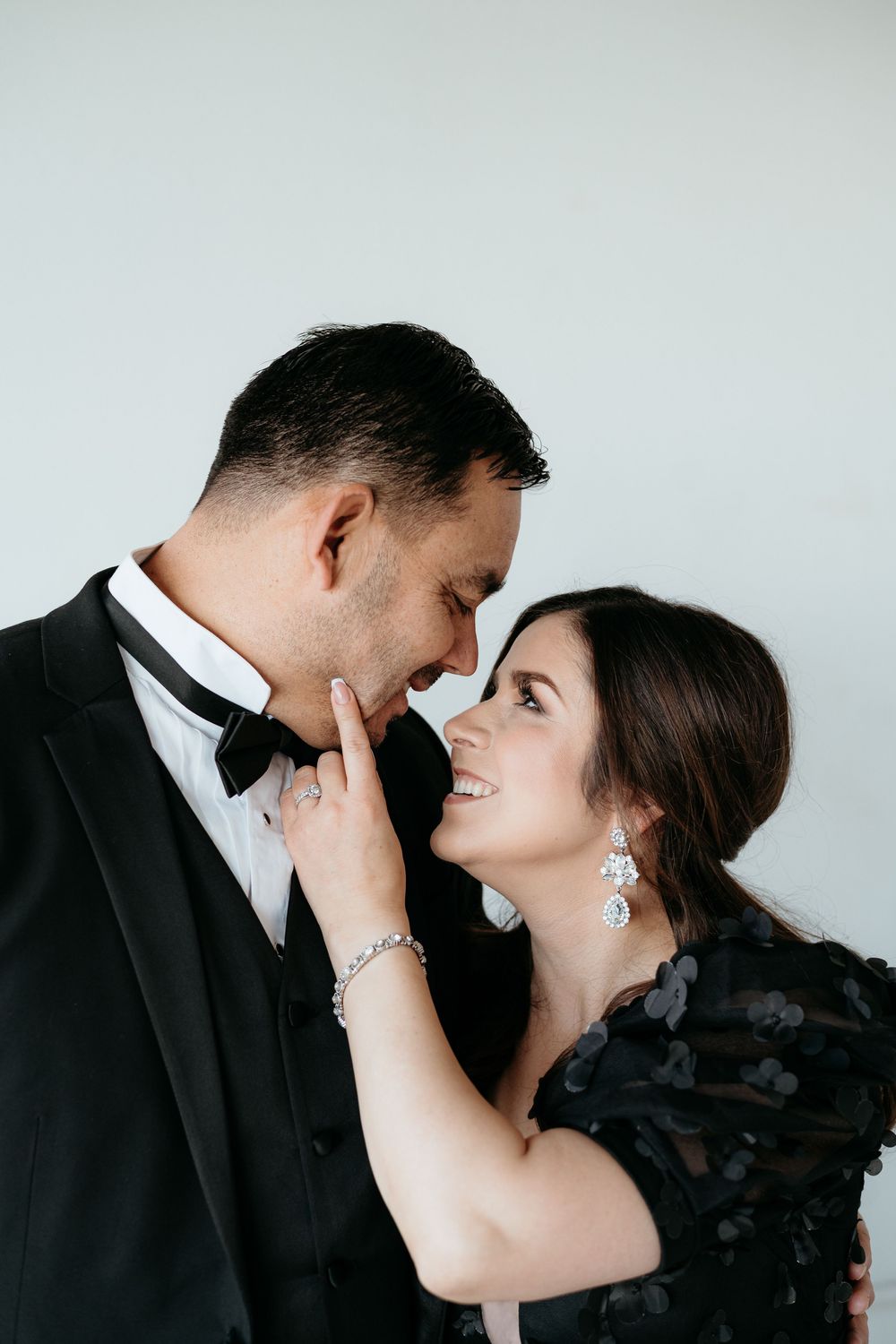 Couple in formal wear share tender moments against white backdrop during photoshoot.