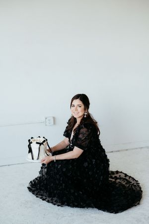Woman in elegant black gown poses gracefully on white floor during studio photoshoot.