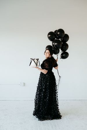 Woman in dramatic black gown creates artistic poses with black balloons.