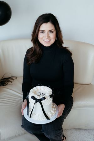 Woman in black turtleneck holds white celebration cake with number 35.