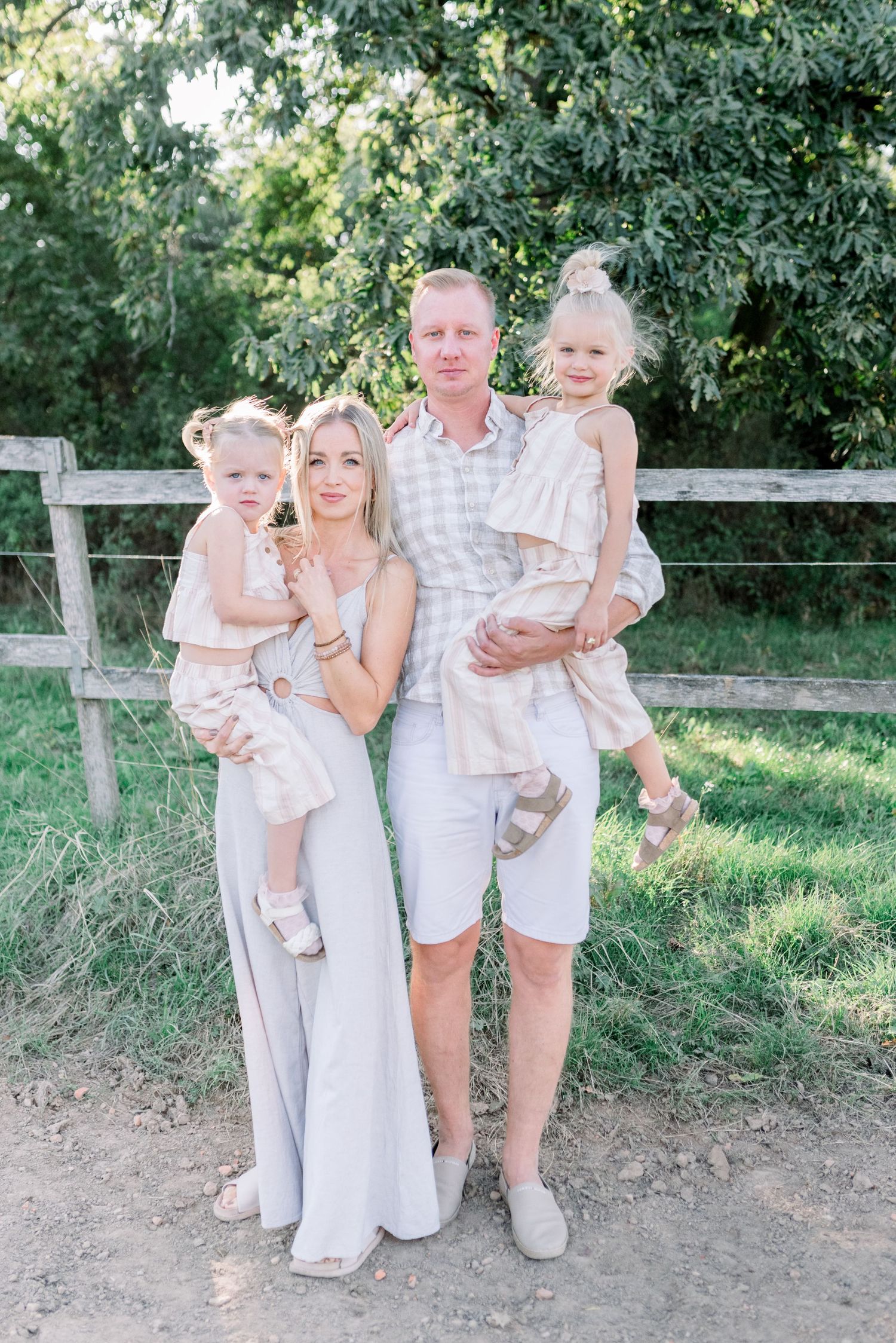 Family group poses together outdoors wearing coordinated white and neutral outfits.