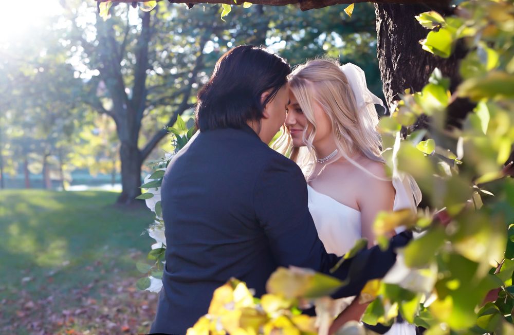 A romantic wedding couple shares tender moments under golden autumn foliage in a park setting.