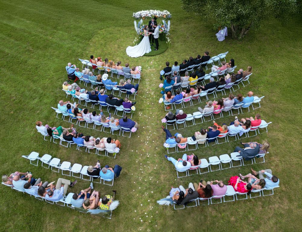 drone shot of wedding ceremony,  guests seated in curved rows on a manicured lawn.