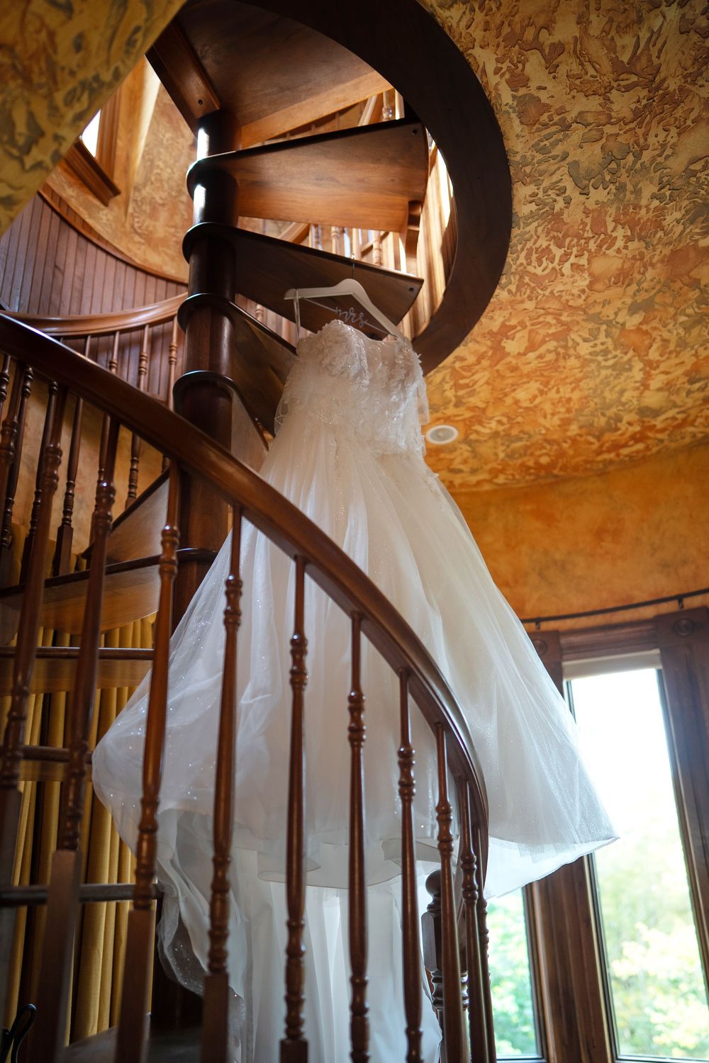 White wedding dress draped over elegant wooden spiral staircase in ornate vintage interior.