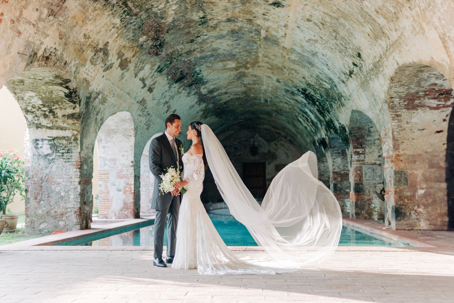 Wedding photos captured under rustic stone archways with dramatic veil movement.