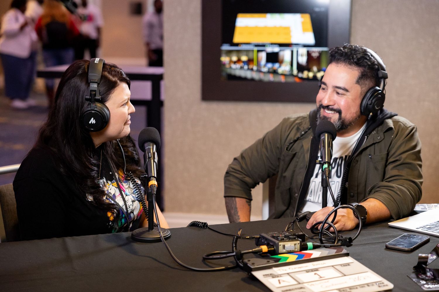 Man and woman wearing headphones recording a podcast at a table with microphones at a conference.