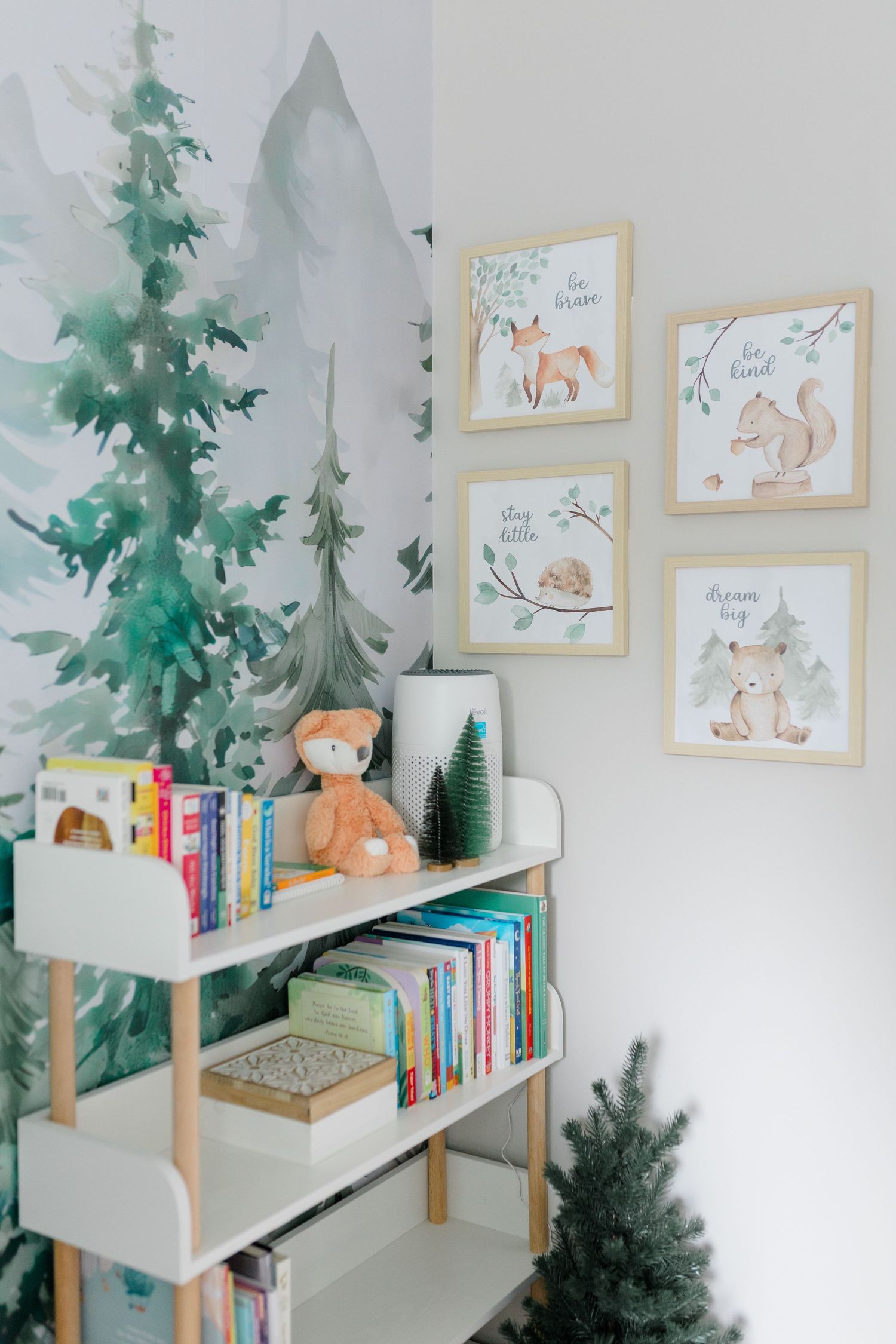 Woodland-themed nursery with green tree mural, white shelving, and framed animal artwork.