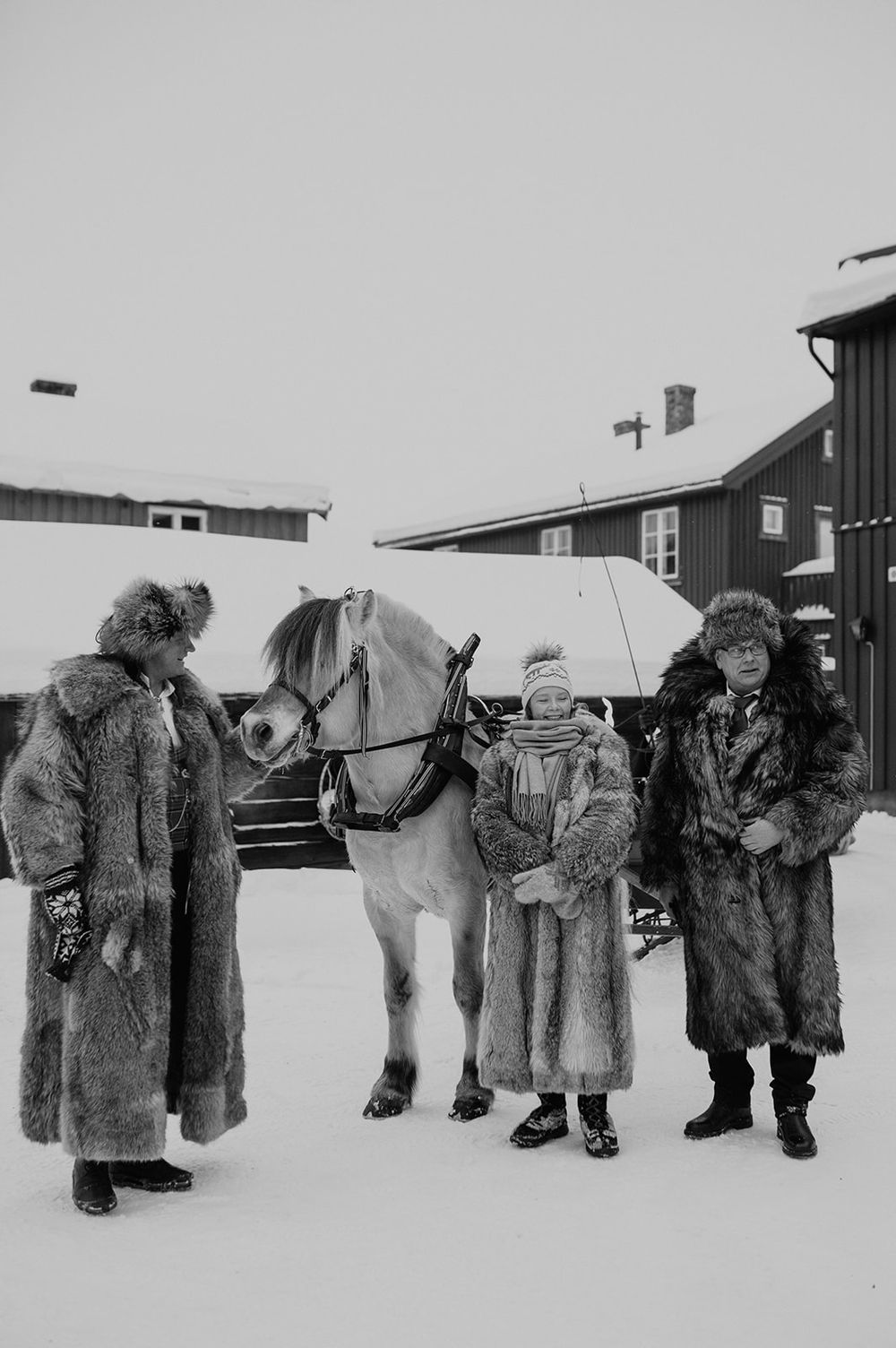 A group of figures wearing heavy winter fur coats and boots stand in the snow beside their sled dogs in Antarctica.