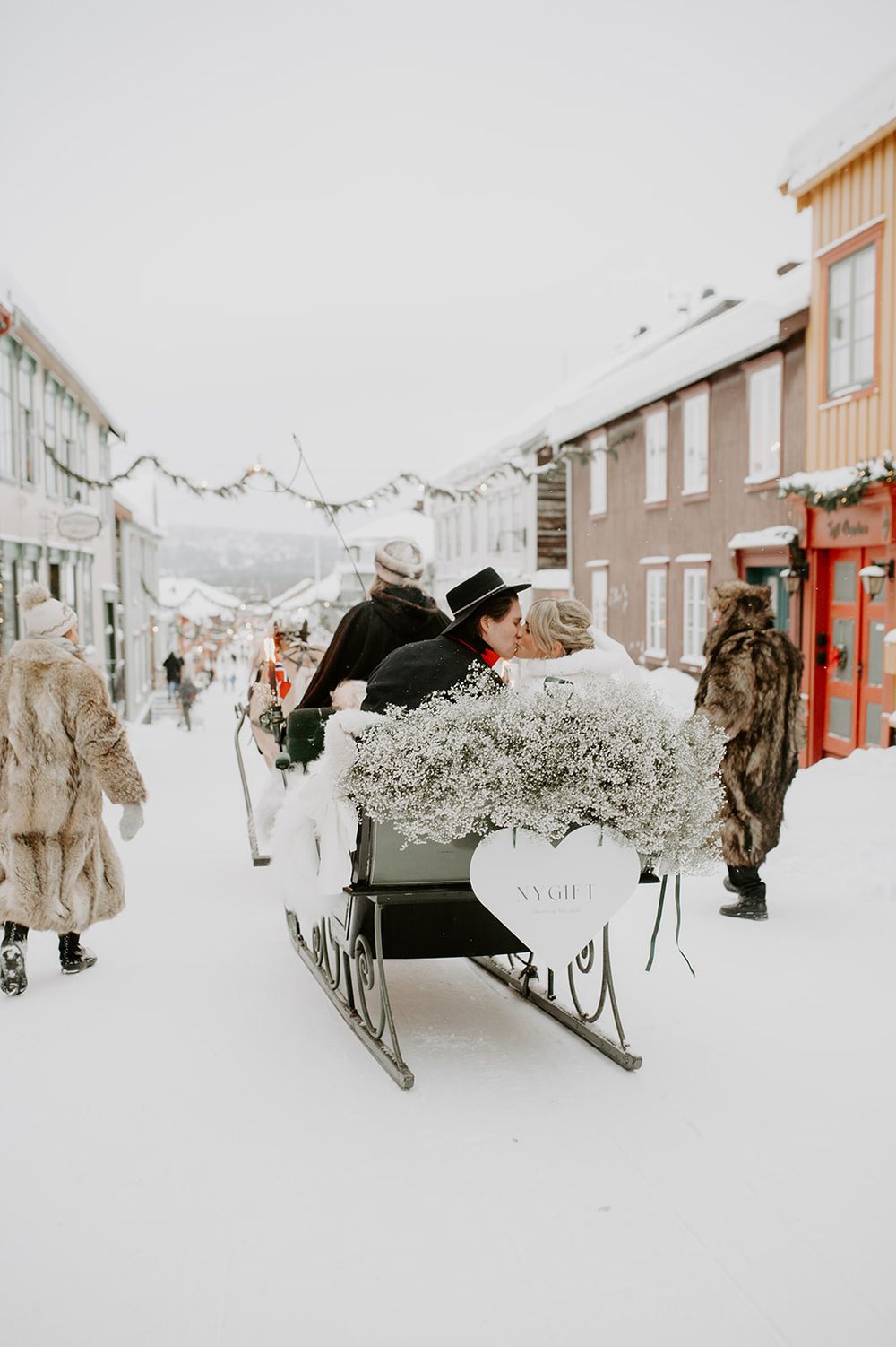A snowy winter street scene with a horse-drawn sleigh ride in a northern town.